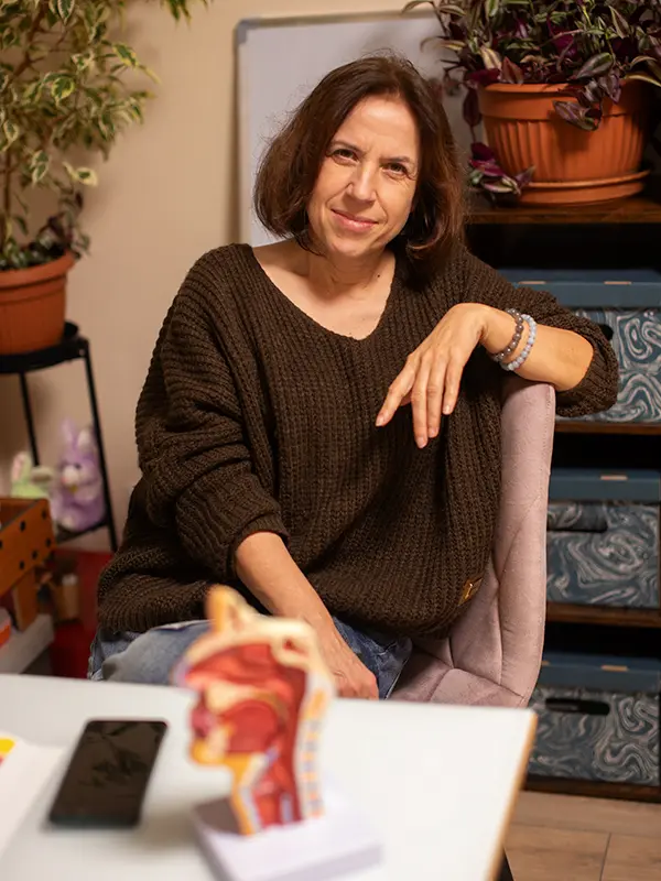 Kobieta w przytulnym swetrze siedzi w domowym biurze, na stole stoi model ludzkiego gardła.