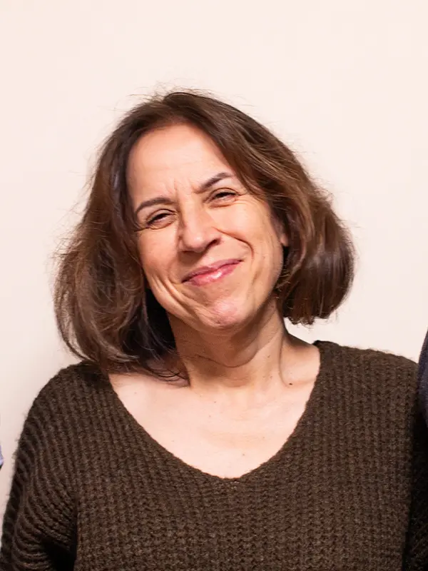 Osoba z krótkimi brązowymi włosami, uśmiechnięta, ubrana w brązowy sweter na jednolitym tle.