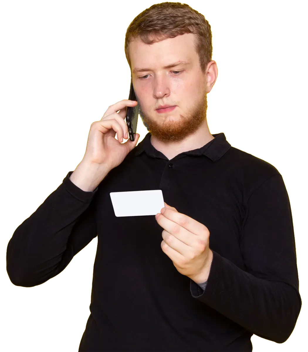 Mężczyzna w czarnej koszuli rozmawia przez telefon, trzyma białą kartę i ma skupiony wyraz twarzy.